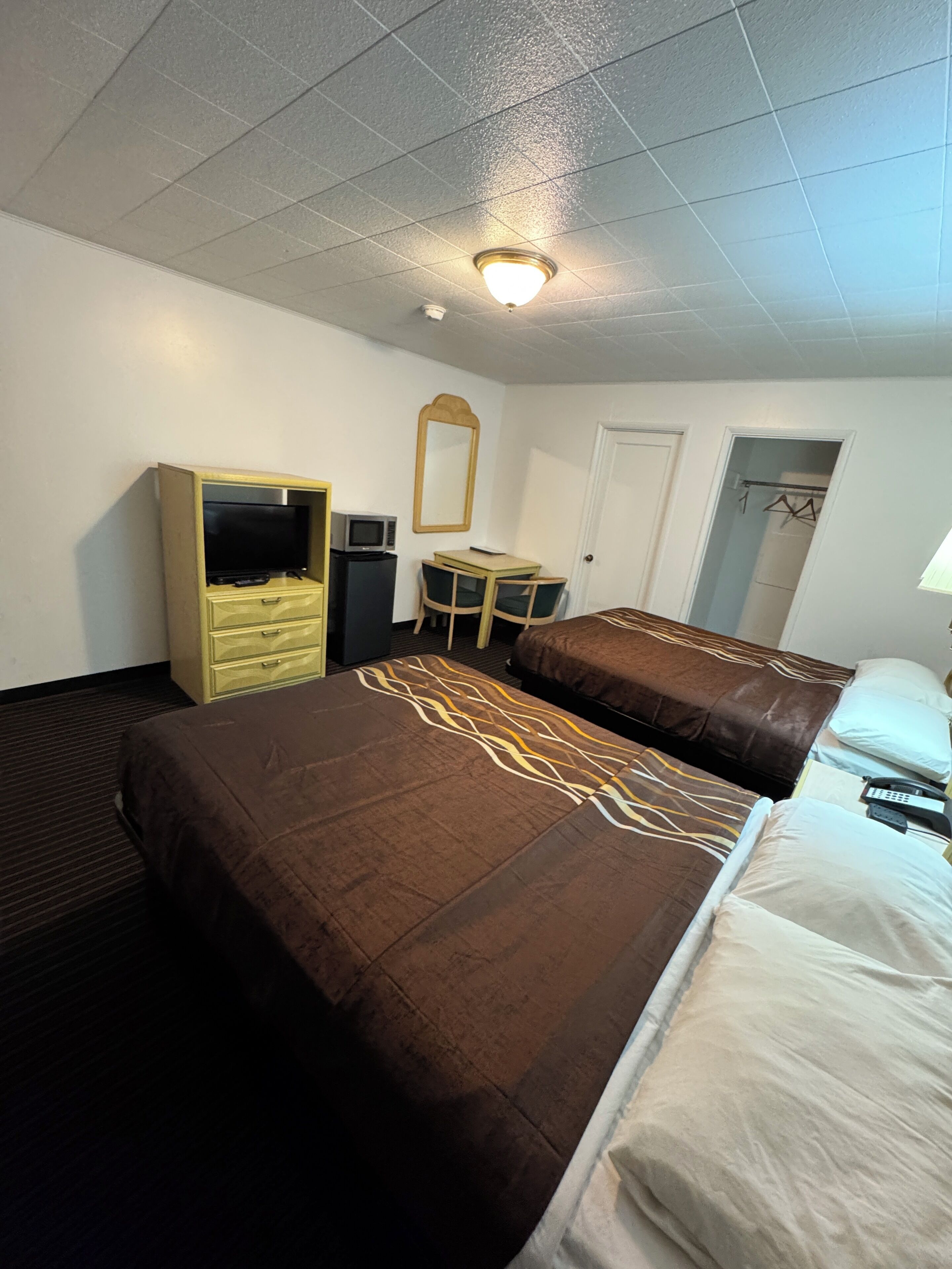 Una habitación de hotel con cama, escritorio, televisión, espejo y armario.