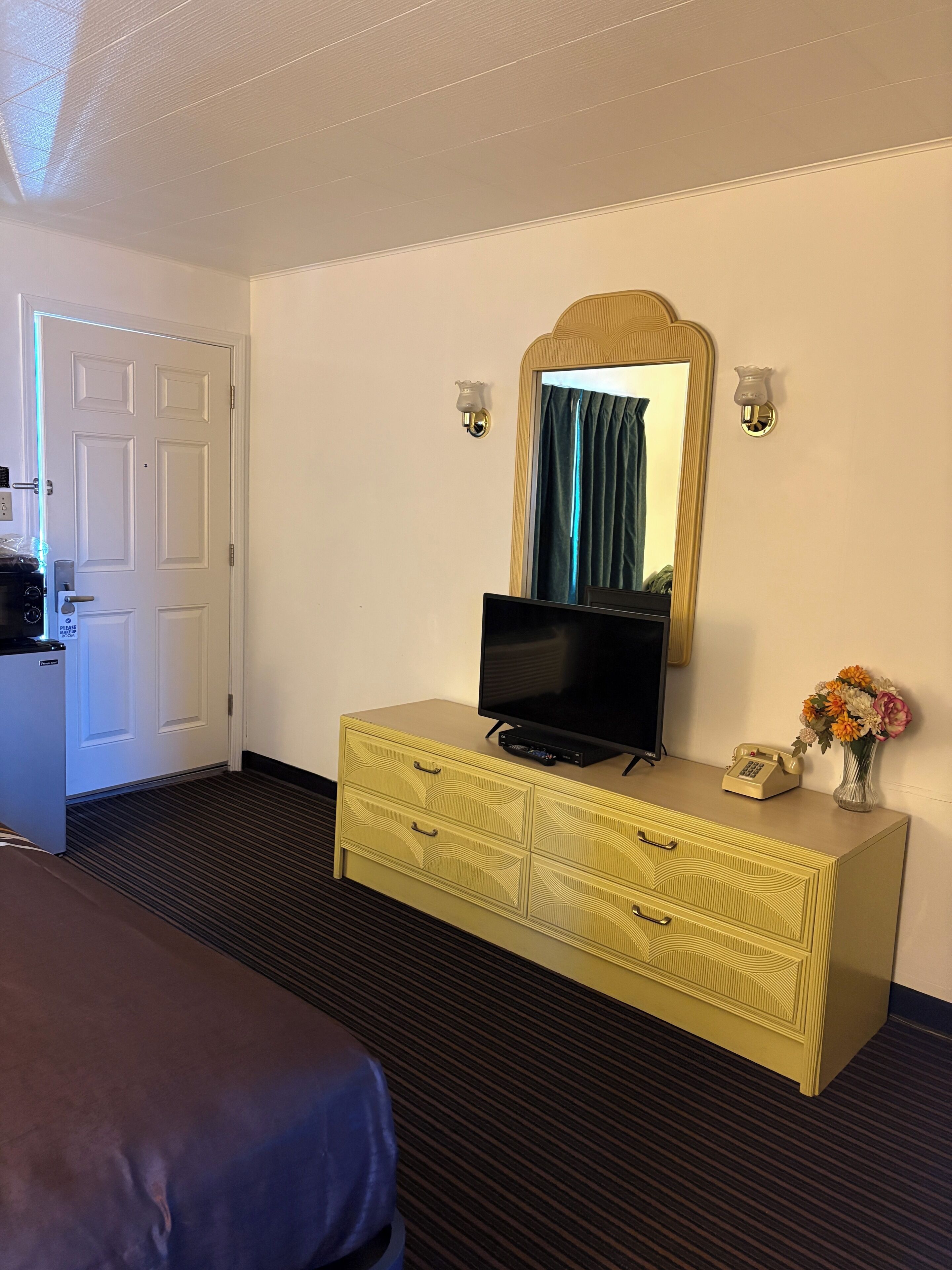 A hotel room with a bed, a television on a dresser, a mirror, and a telephone.