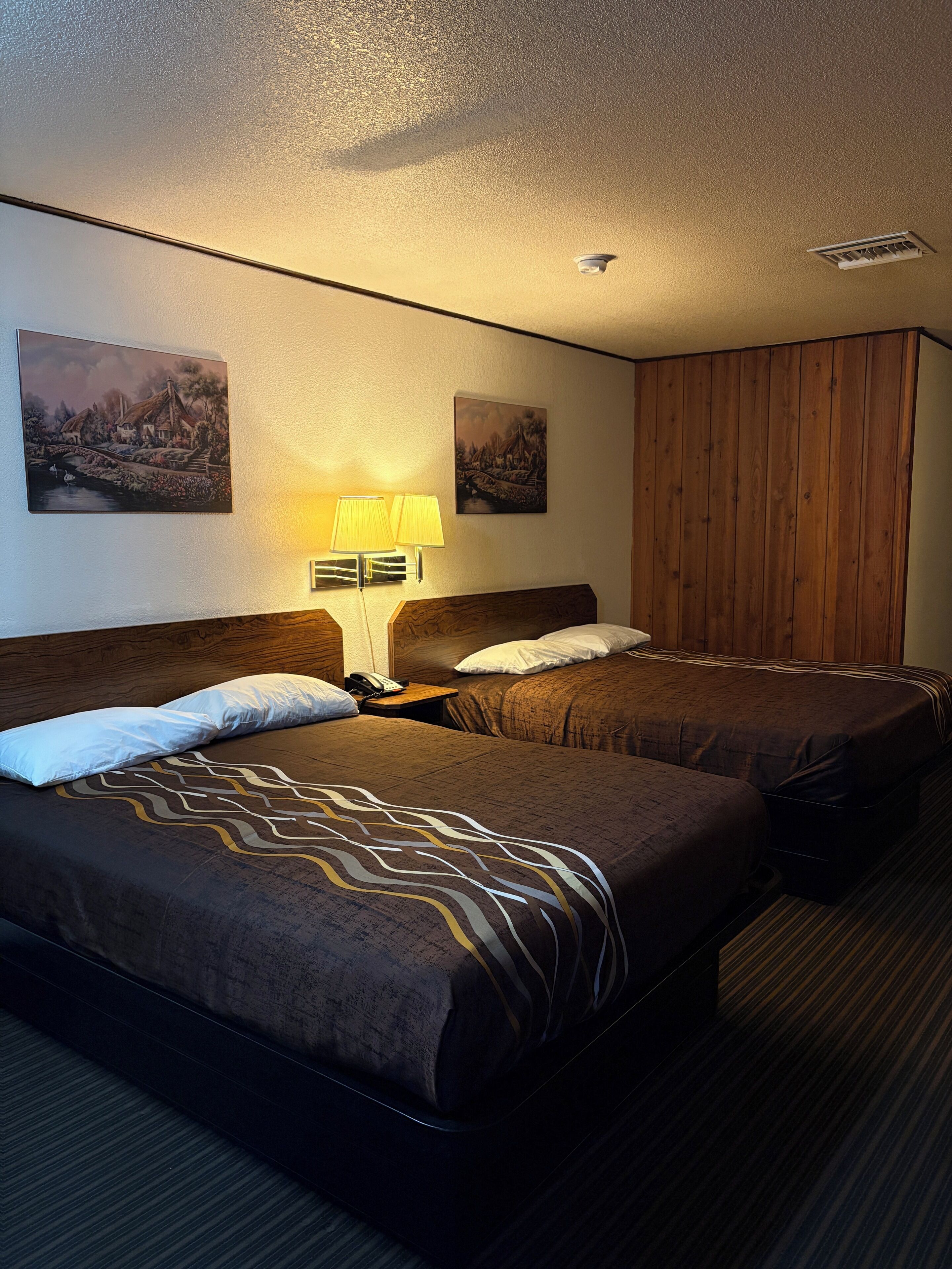 Ein Hotelzimmer mit zwei Betten, einem Holzschrank und zwei Wandlampen.
