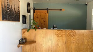 A reception area with a wooden counter, a wall-mounted phone, a painting, and a sliding door. - Motel Garberville (Garberville)
