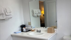 A bathroom with a white sink, mirror, and toilet. There are towels hanging on the wall, a trash bin, and a basket on the counter. - Motel Garberville (Garberville)