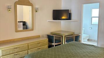 Habitación de hotel con cama, televisor sobre un mueble bajo, escritorio, silla, cómoda y espejo.