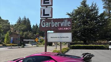 A motel sign with 'MOTEL' spelled out in blocks, a 'Garberville' sign below, and a pink sports car parked in front.