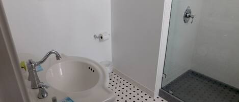 Un baño con lavamanos blanco, cabina de ducha de vidrio y suelo de baldosas.