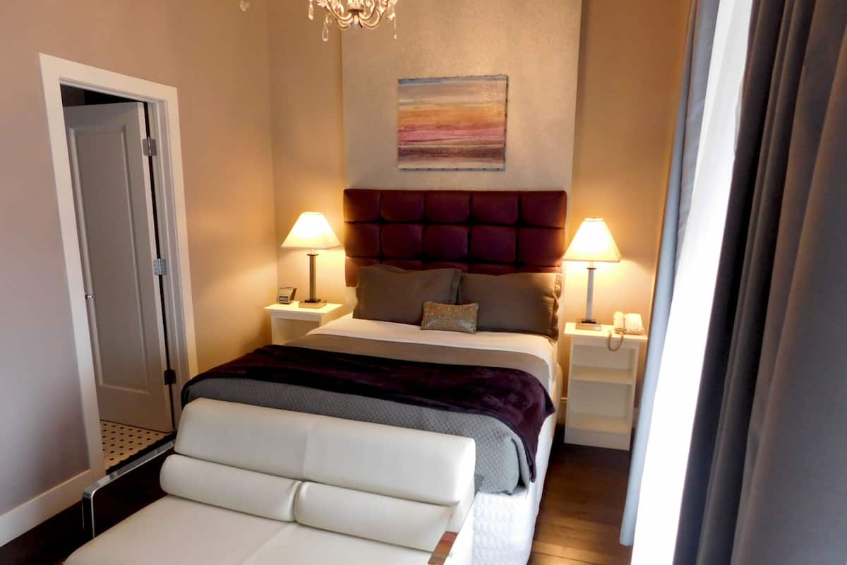 A hotel room with a bed, two bedside tables, a nightstand, a chair, and a chandelier.
