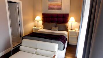 A hotel room with a bed, two bedside tables, a nightstand, a chair, and a chandelier.