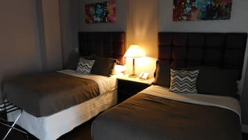 Quarto de hotel com duas camas, uma mesa de cabeceira com abajur, e duas pinturas abstratas nas paredes.
