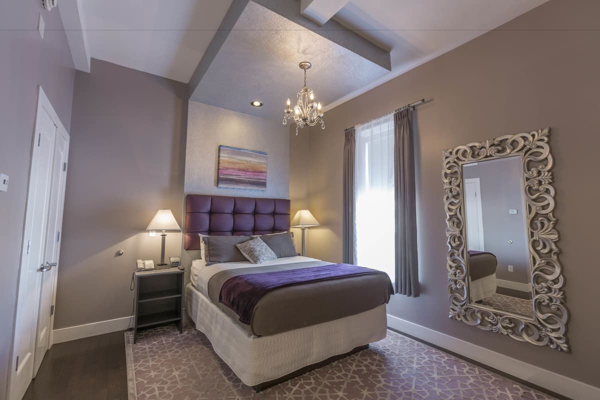 A bedroom with a large bed, a chandelier, a decorative mirror, and a painting on the wall.