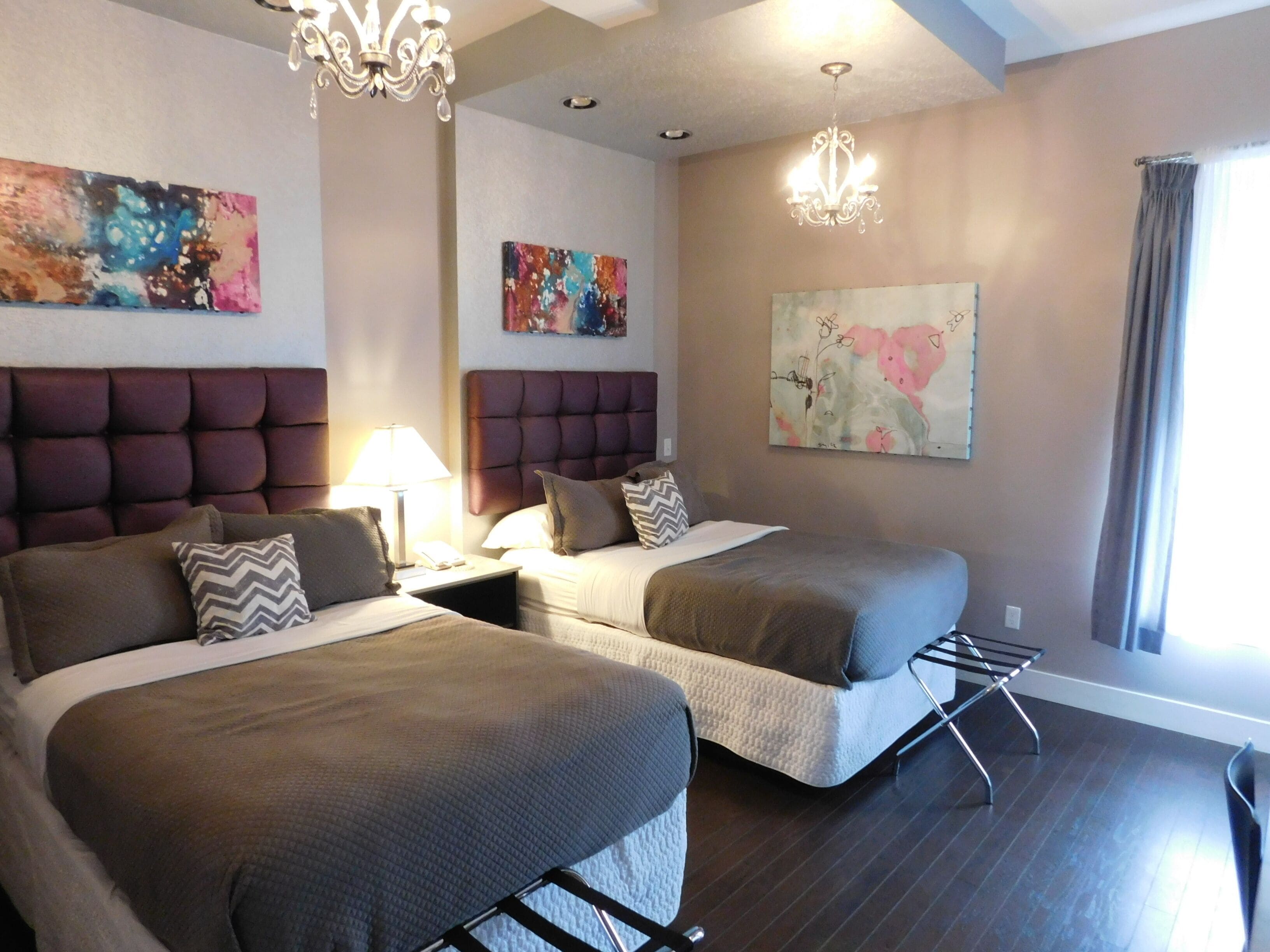 Habitación de hotel con dos camas, un candelabro, obras de arte en las paredes y una ventana con cortinas.