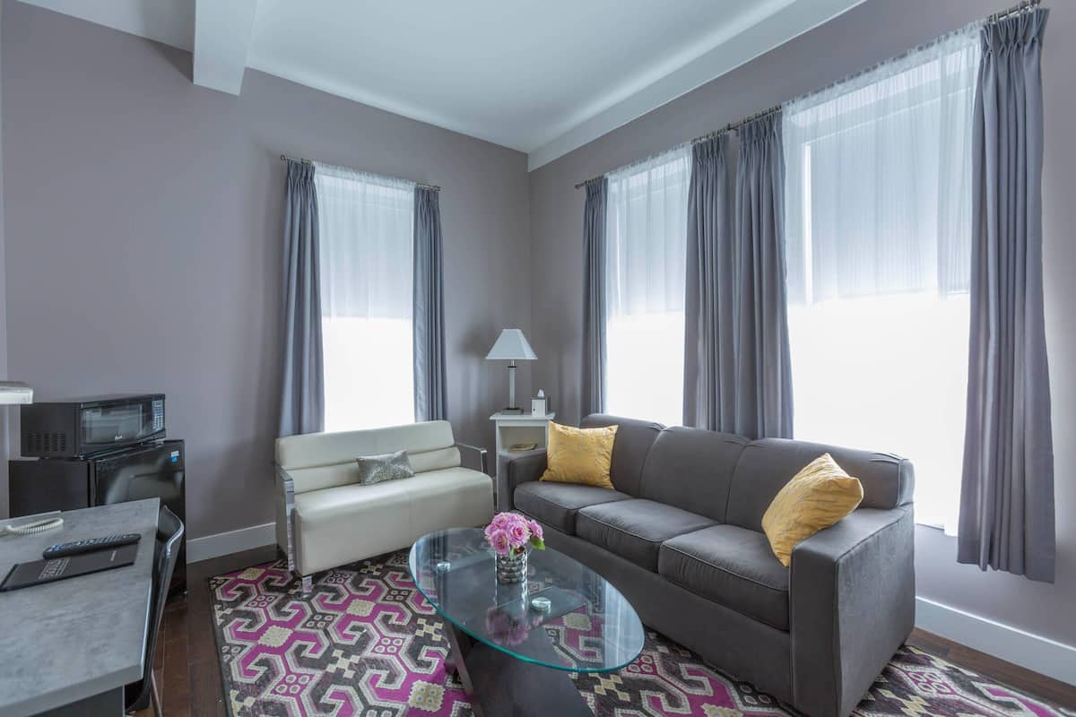 A modern living room with a sofa, a glass coffee table, a white armchair, and a patterned rug.