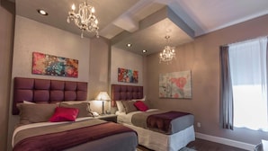 Une chambre d’hôtel avec deux lits, un lustre, des œuvres d’art accrochées aux murs et une fenêtre avec des rideaux.