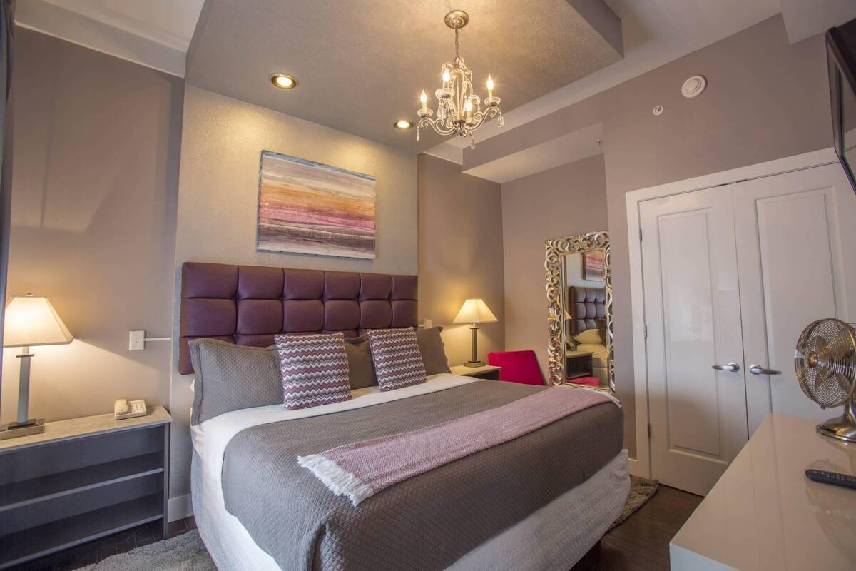 A bedroom with a large bed, two bedside tables with lamps, a chandelier, a wardrobe, and a mirror.