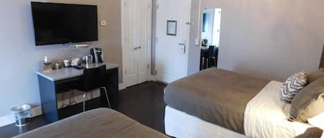 A hotel room with two beds, a desk with a computer, a flat-screen TV, and a chandelier.