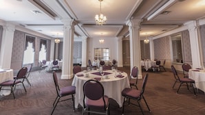 Une salle de banquet avec des tables rondes, des chaises, des lustres et des colonnes.