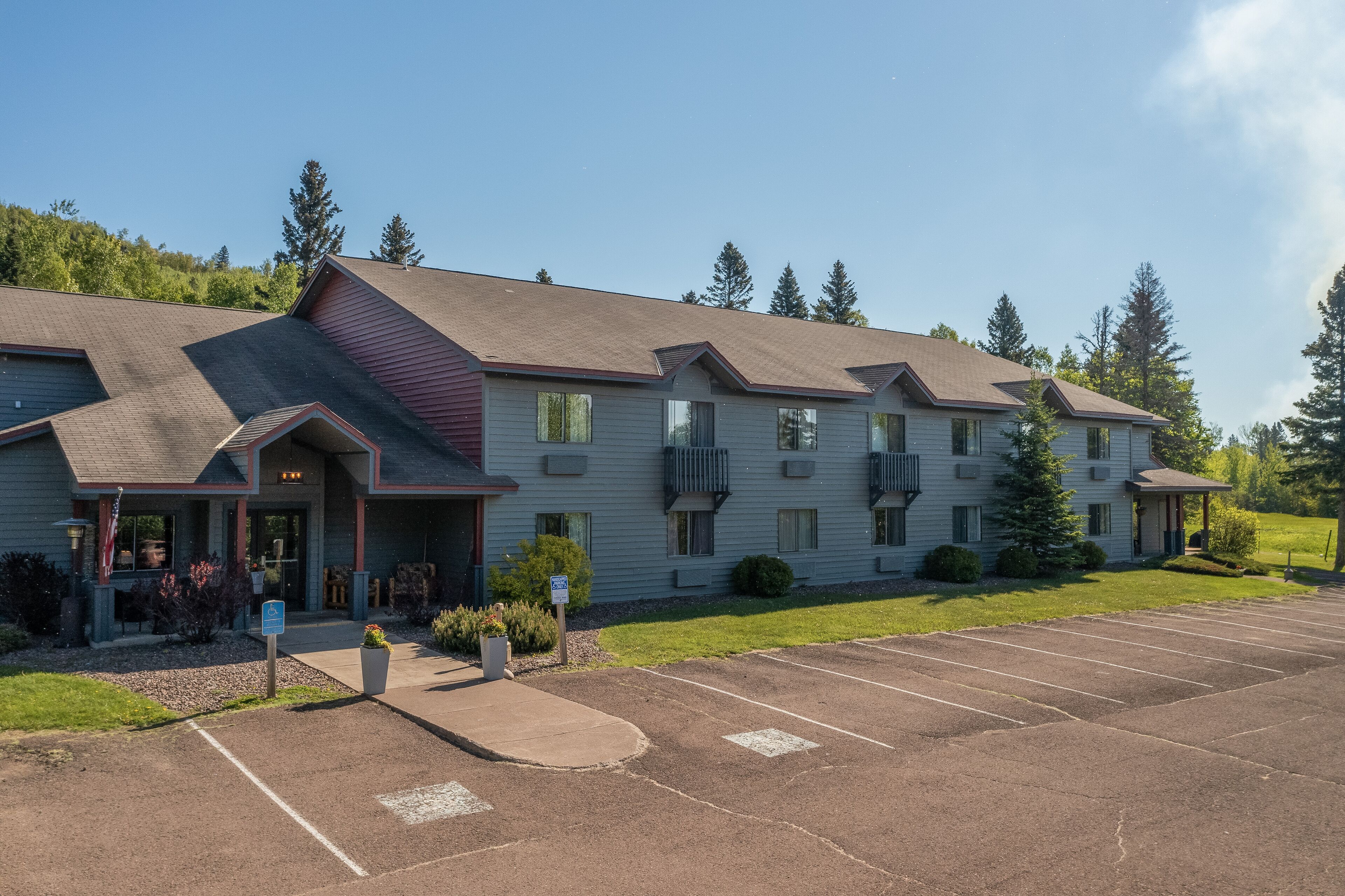 A multi-story hotel with a parking lot and a grassy area with trees.