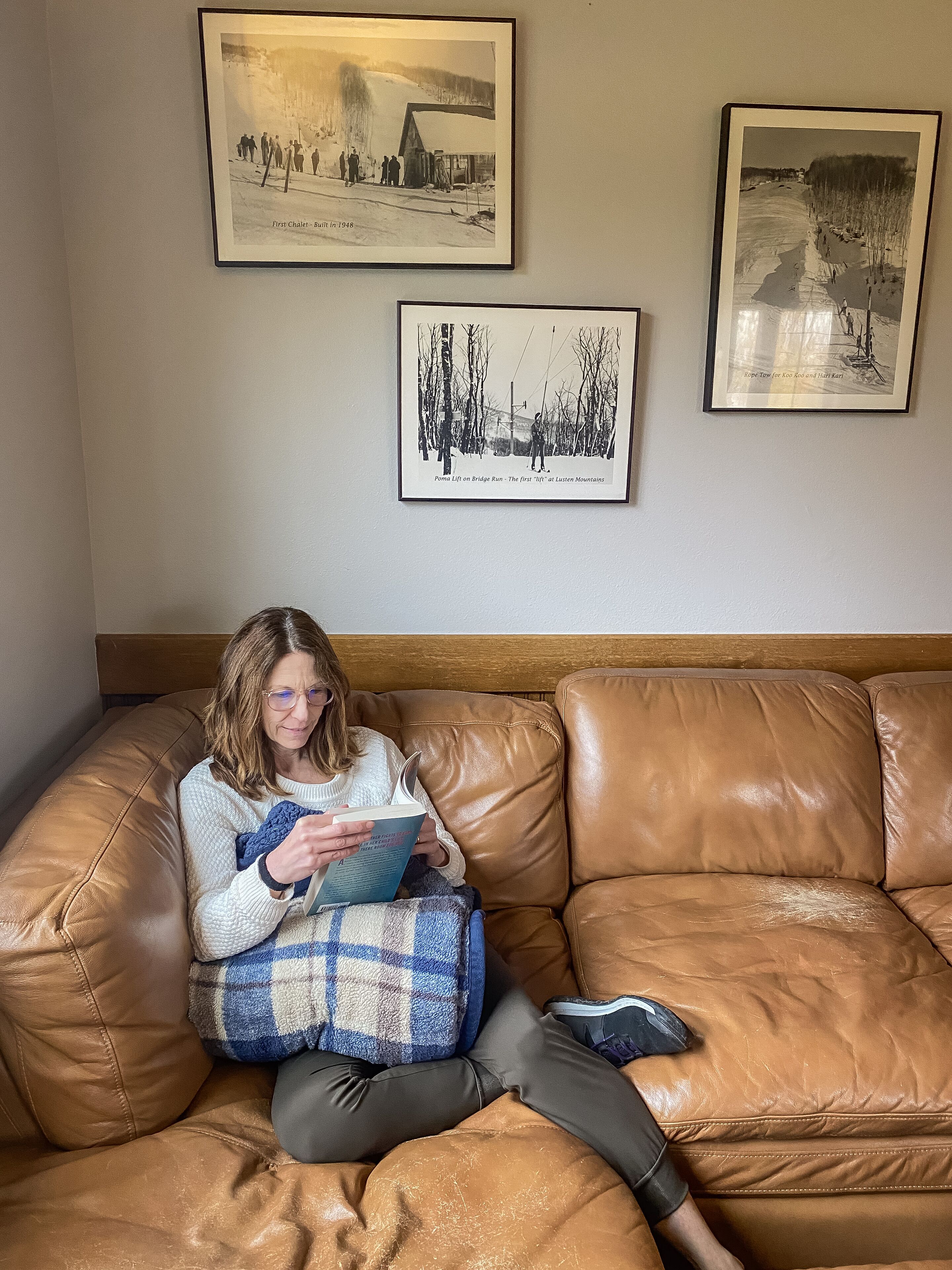 A person sitting on a brown leather couch in a room with three framed photographs on the wall.