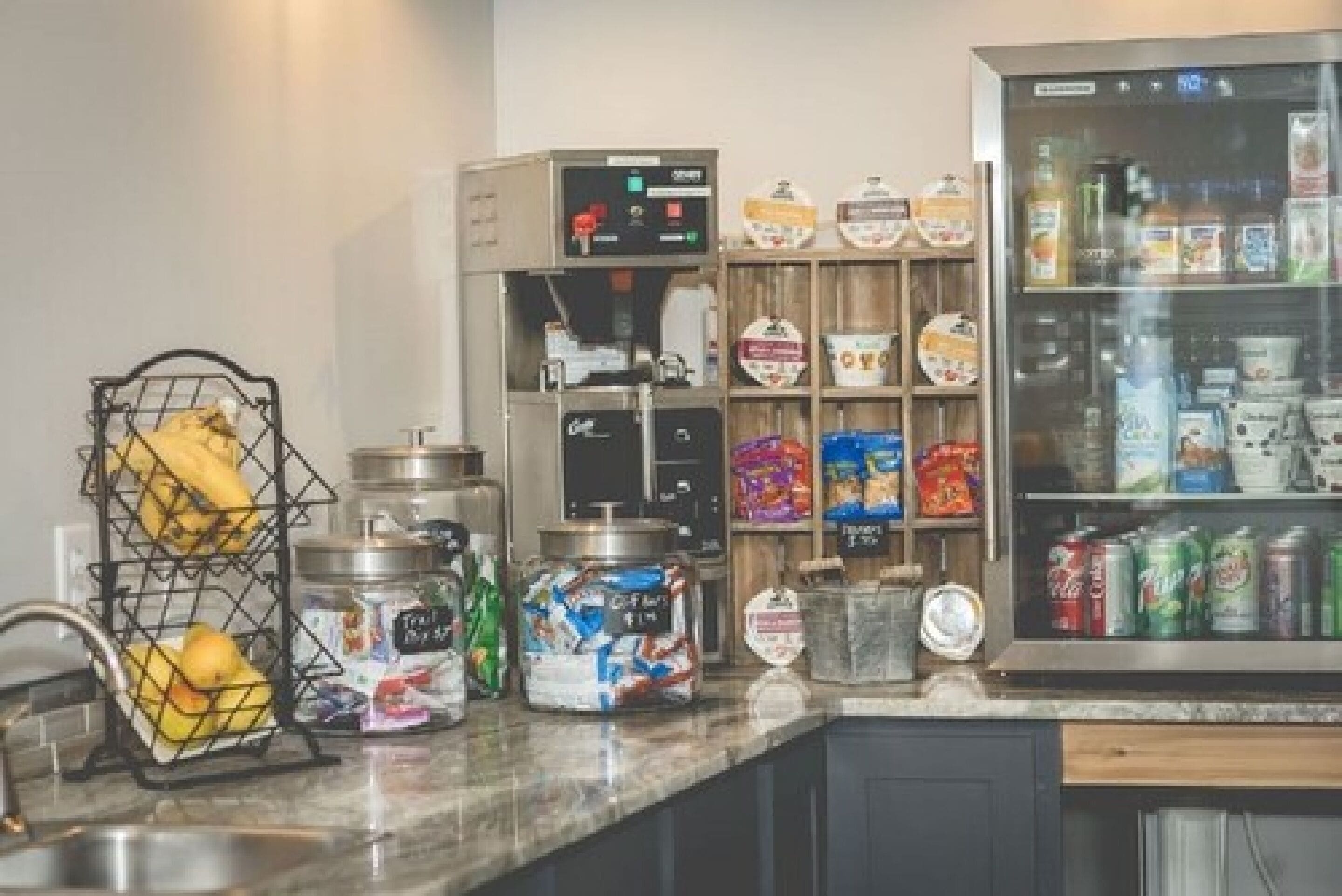 A kitchen with a coffee machine, a fruit basket, and various food items on the counter.