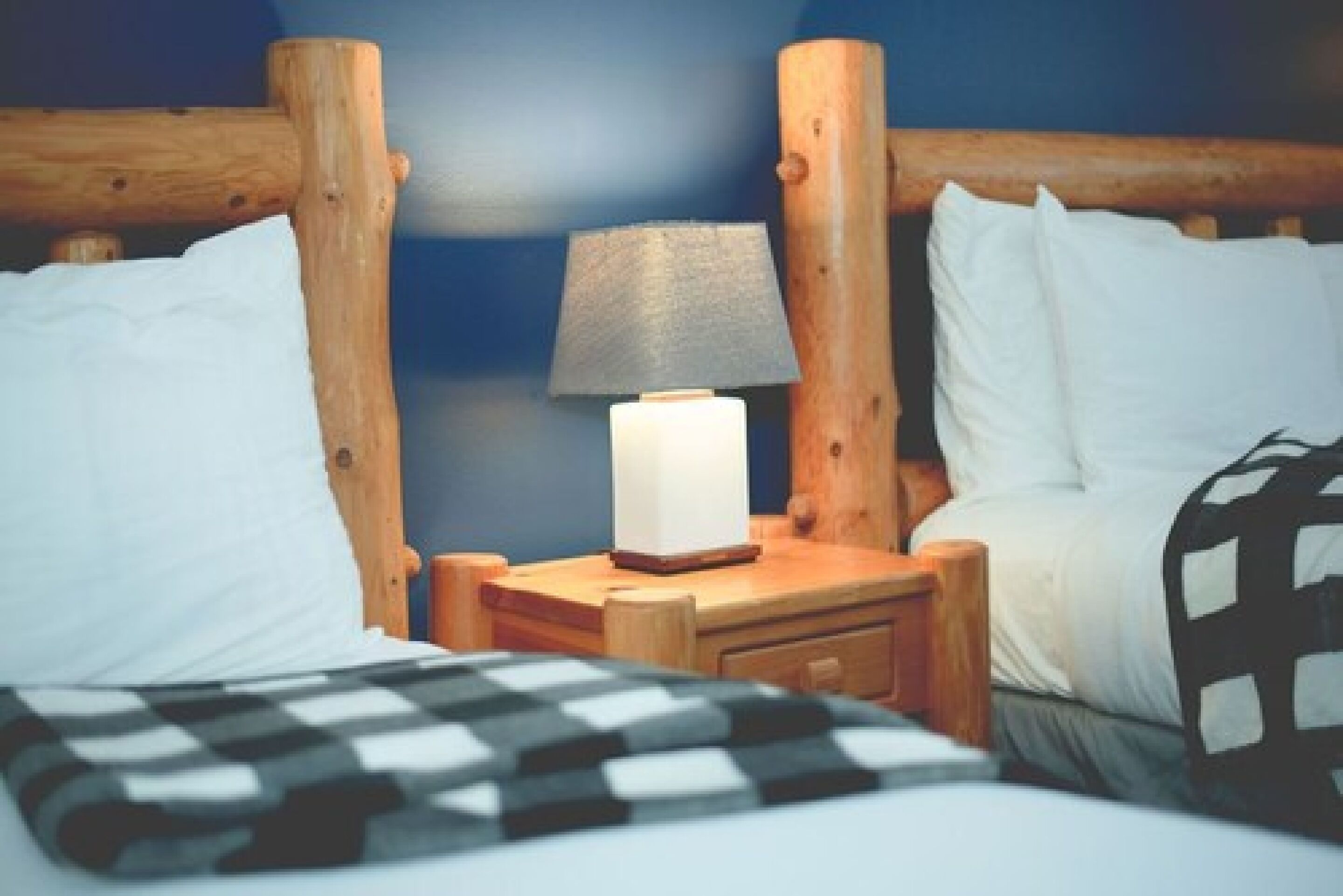 A wooden headboard with a nightstand, a lamp, and a bed with white pillows.