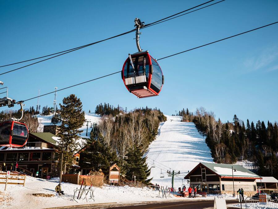 A ski lift with cabins, a snow-covered slope, and buildings with ski lifts.