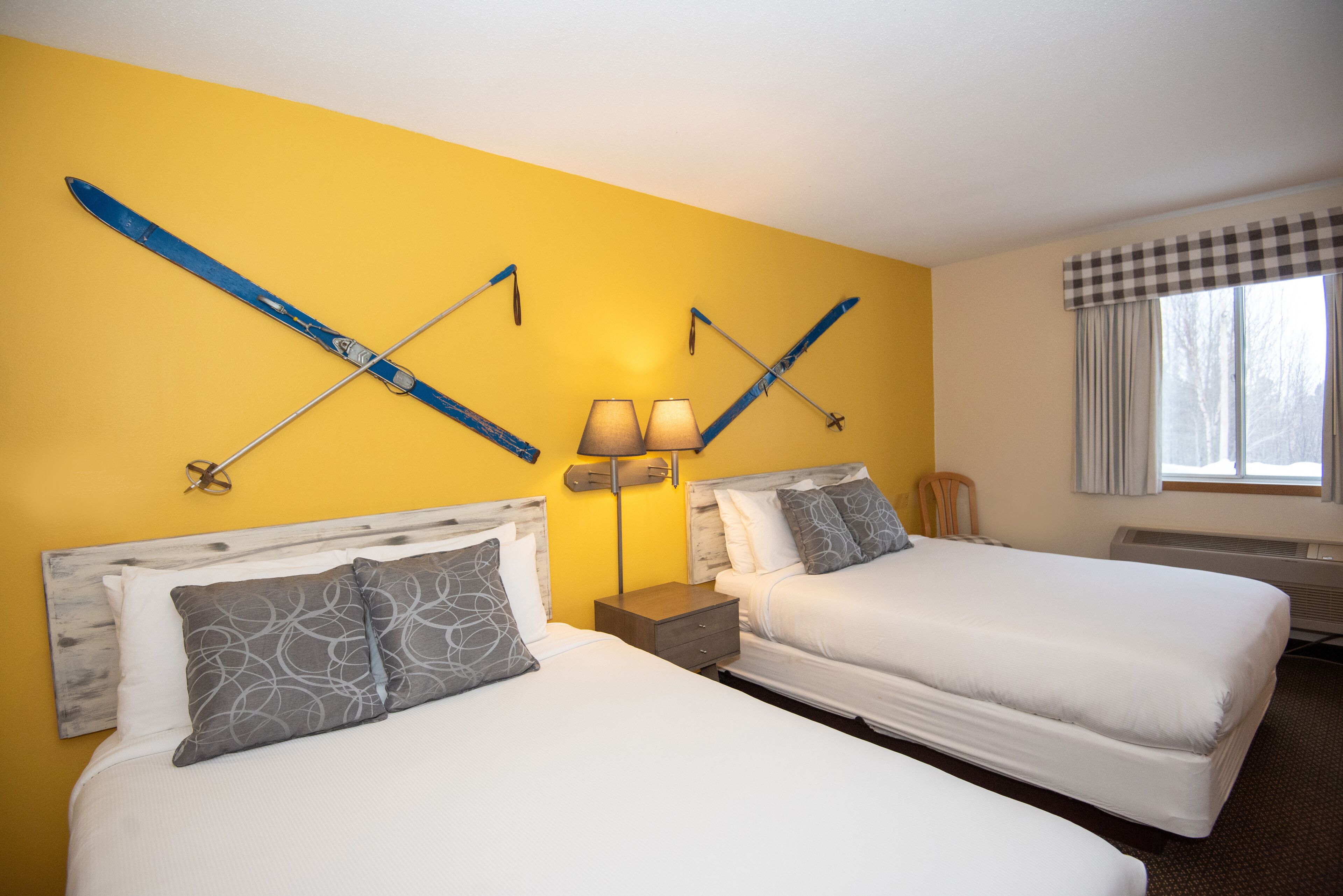 A hotel room with two beds, a checkered window valance, and skis mounted on the wall.