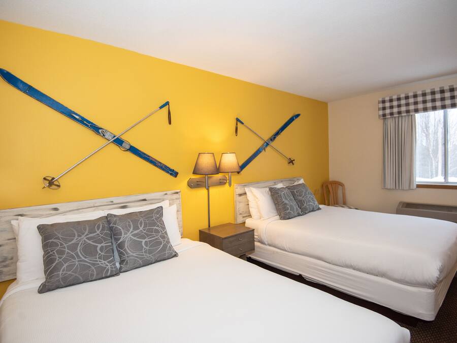A hotel room with two beds, a checkered window valance, and skis mounted on the wall.