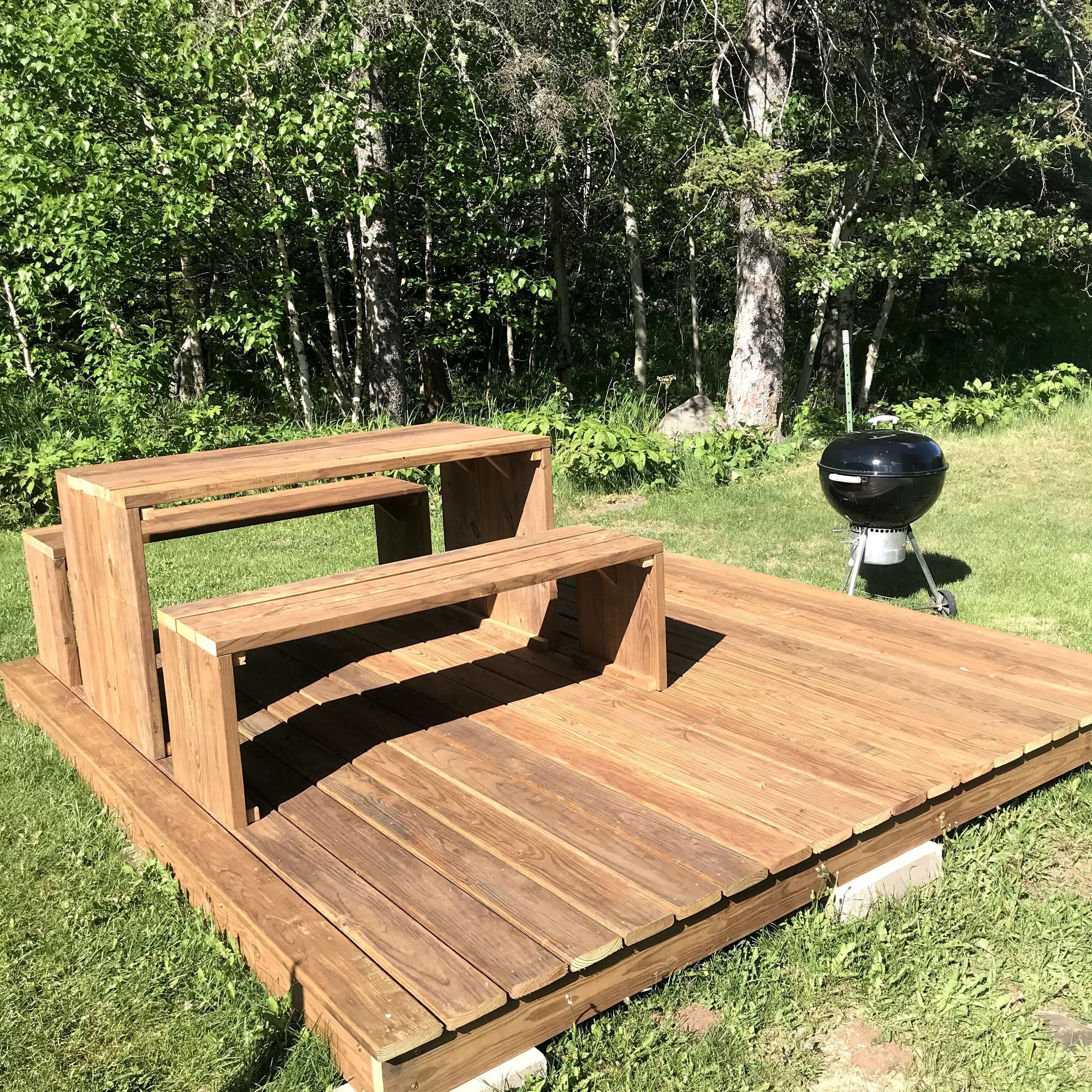 Une table de pique-nique en bois, avec des bancs, située dans un espace extérieur verdoyant.