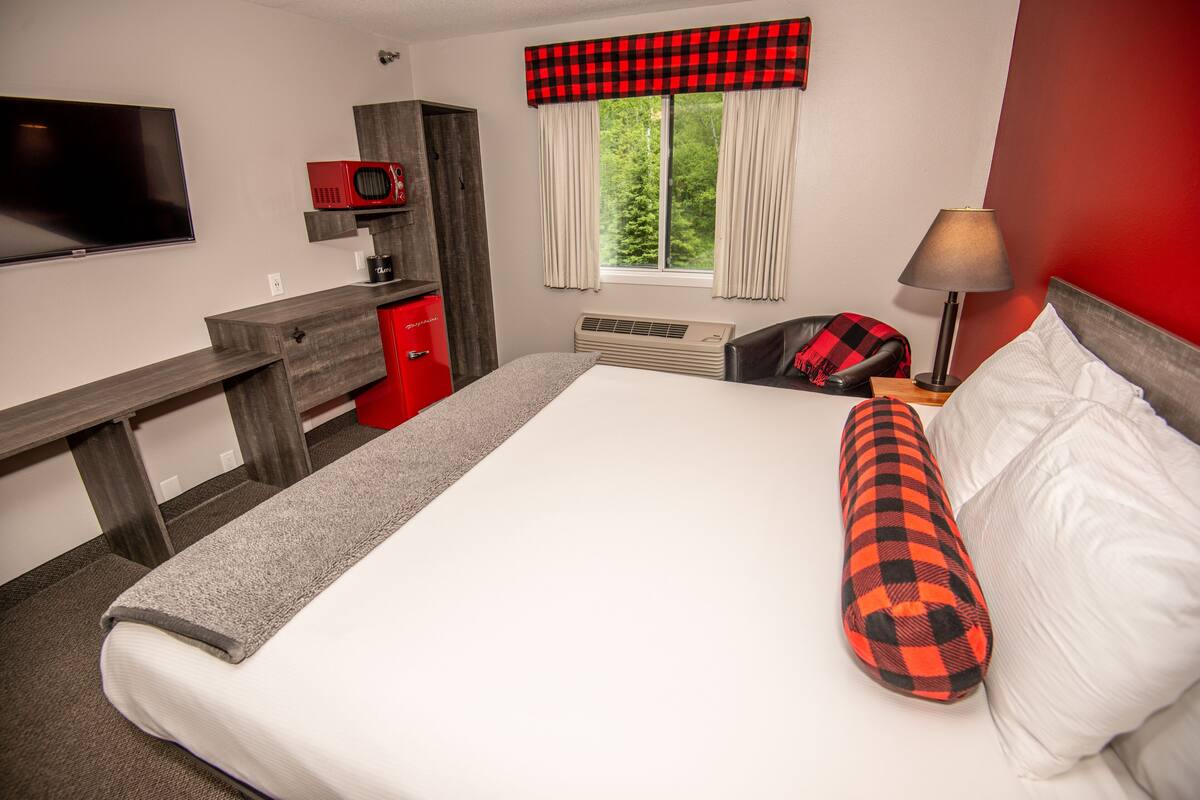 A hotel room with a bed, a desk, a TV, a red cabinet, and a window with curtains.