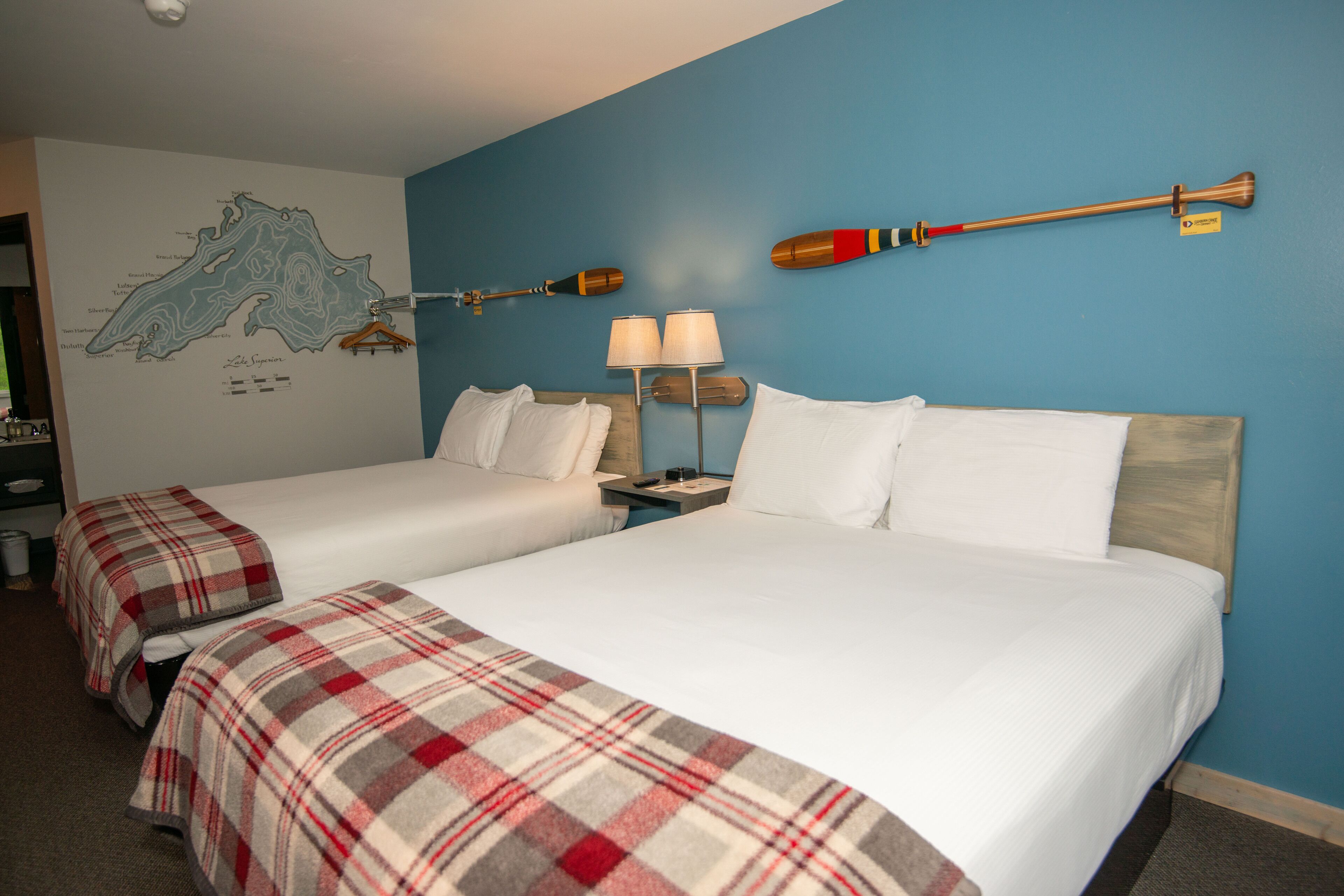 A hotel room with two beds, a map on the wall, and two lamps.