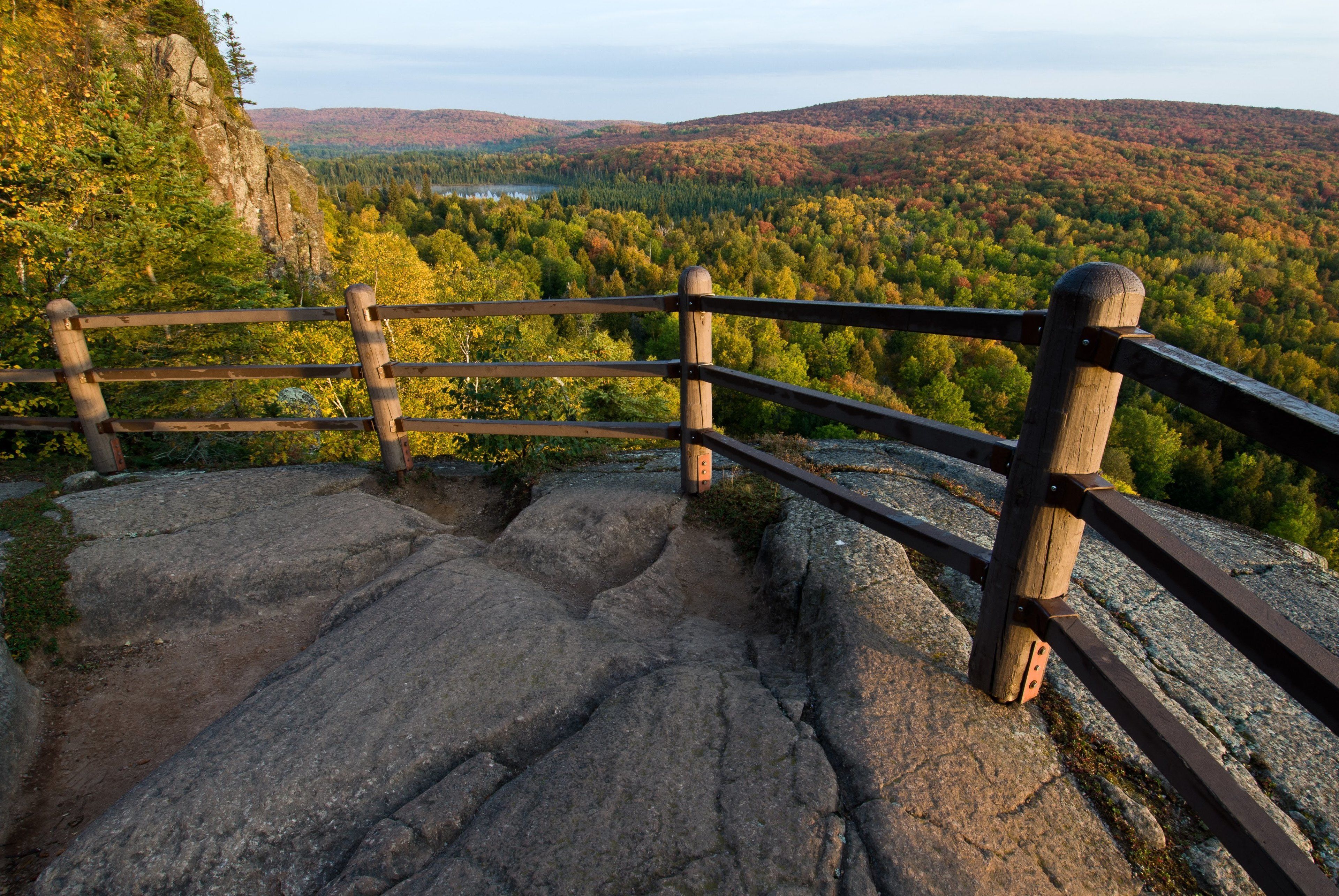 A wooden railing overlooking a forested valley with a lake in the distance.