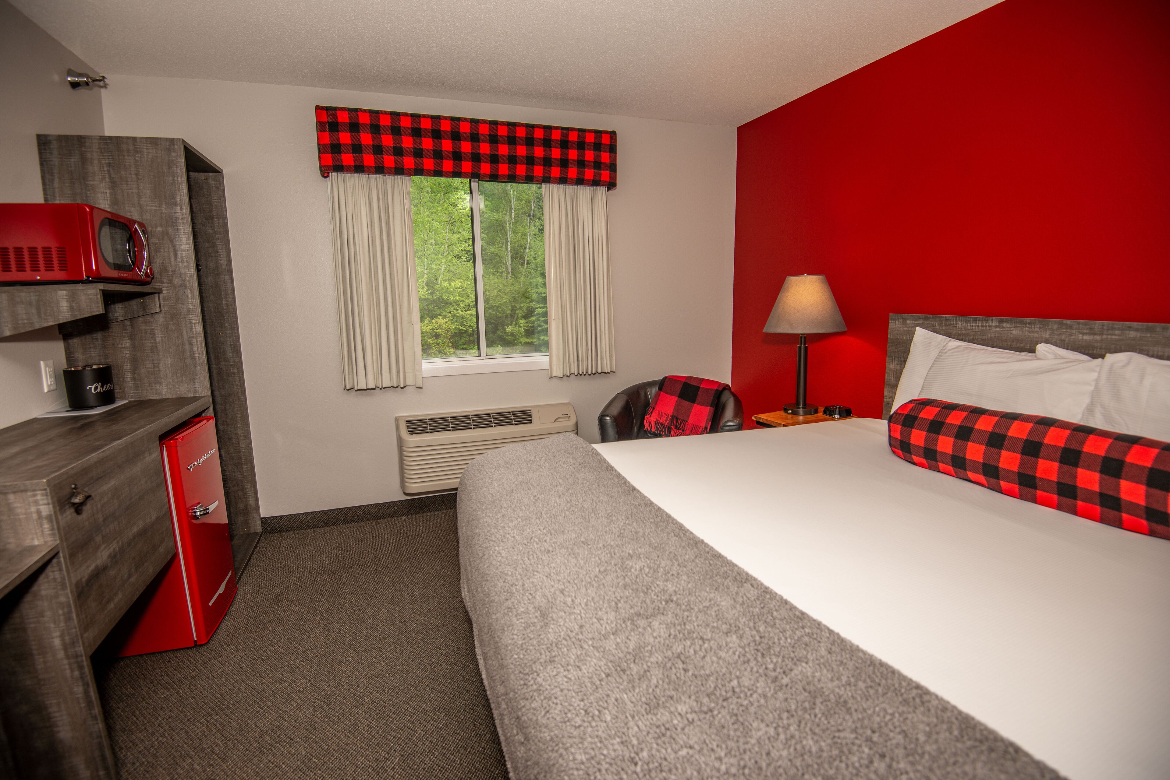 Ein Hotelzimmer mit einem Bett, einem Schreibtisch mit einem roten Radio, einem Heizkörper und einem Fenster mit Vorhängen.