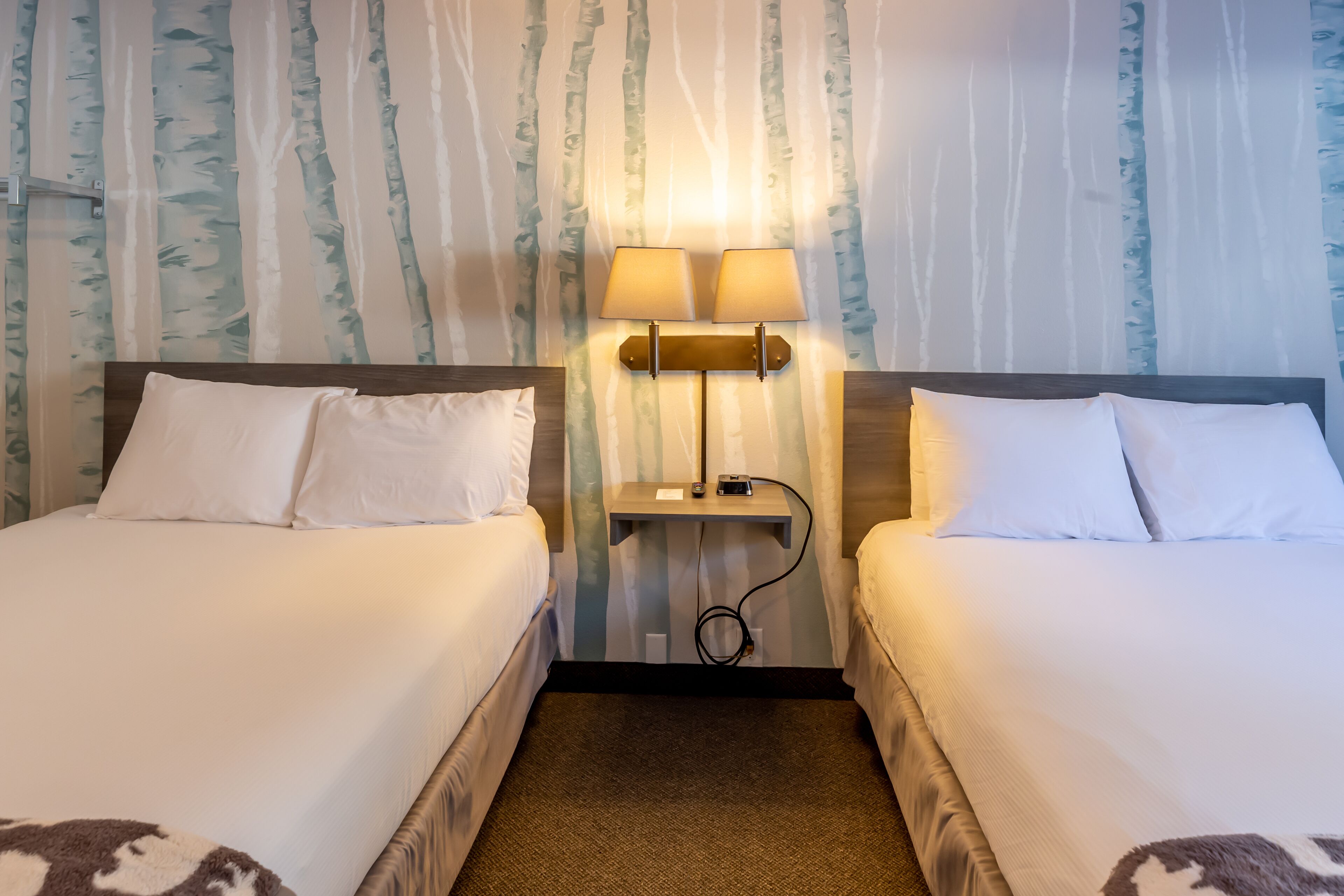 Ein Hotelzimmer mit zwei Betten, einem Nachttisch mit Lampen und einer Wand mit Baummuster.