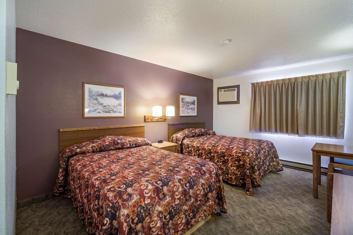 A hotel room with two beds, a window with curtains, and a wall-mounted air conditioning unit.
