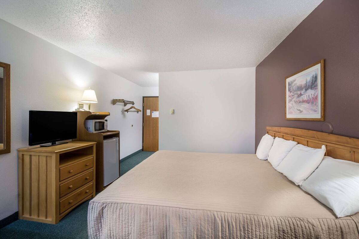 A hotel room with a bed, a TV, a desk with a lamp, and a painting on the wall.