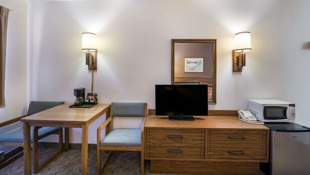 A hotel room with a wooden desk, a television, a microwave, and two wall-mounted lamps. - The Roosevelt Hotel (Wibaux)