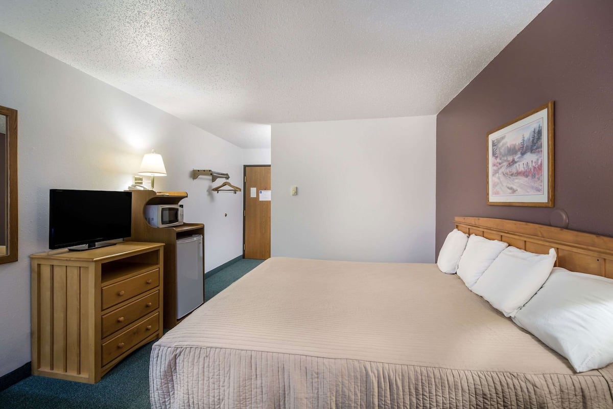 A hotel room with a bed, a TV, a desk with a lamp, and a painting on the wall.