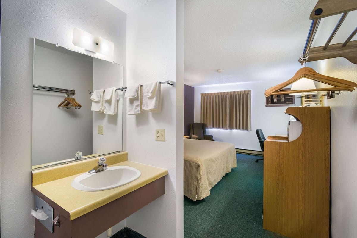 A hotel room with a bathroom, a bed, a desk, and a window with curtains.