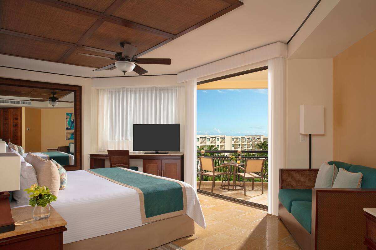 A hotel room with a bed, a television, a desk, and a balcony with a view of the city.