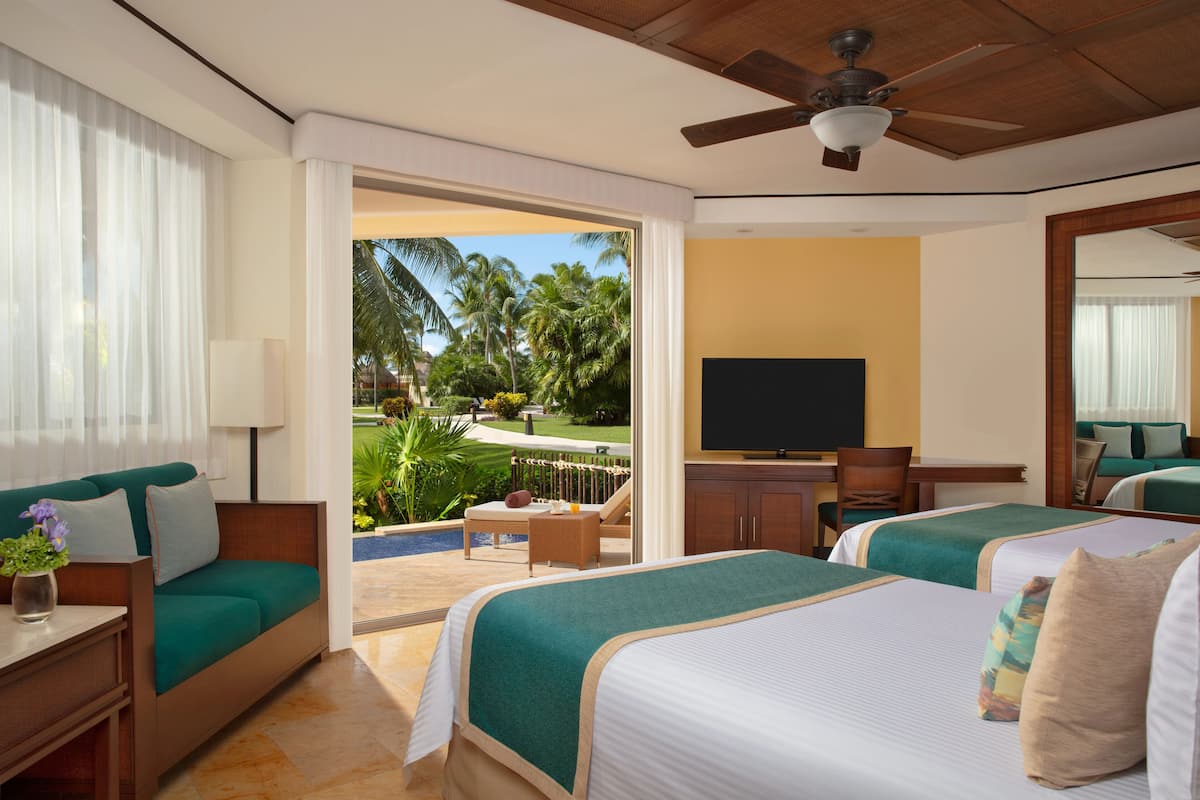 A hotel room with two beds, a TV, a balcony with a view of palm trees, and a ceiling fan.