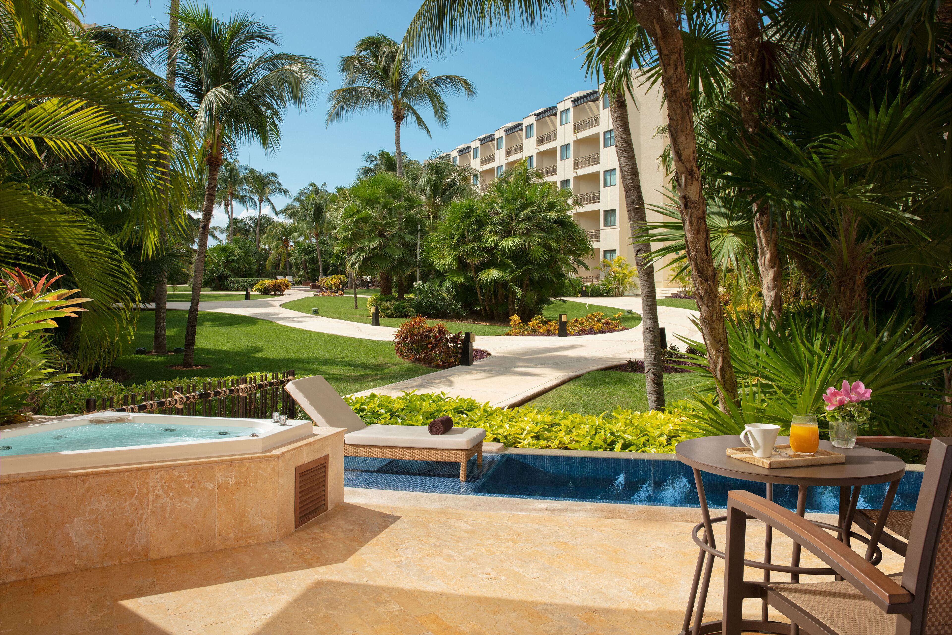 A resort pool area with a hot tub, lounge chairs, and a table with a drink.
