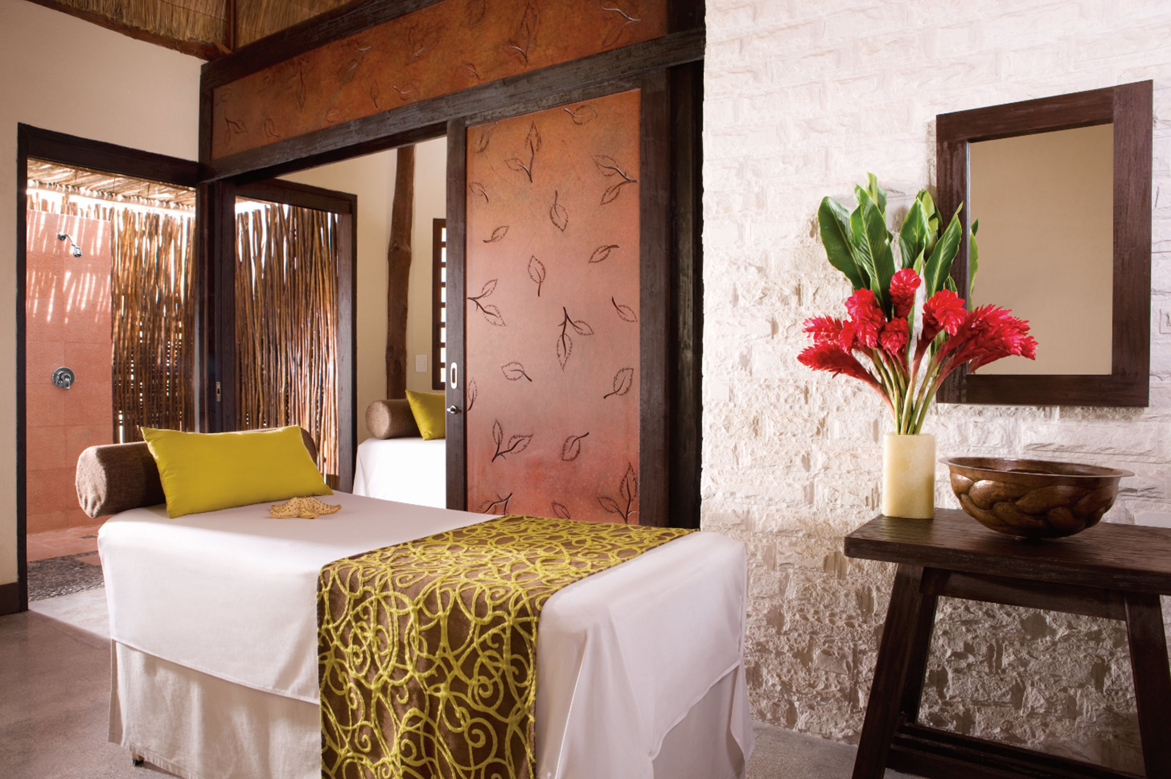 A hotel room with a bed, a bedside table with a vase of flowers, and a mirror on the wall.
