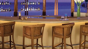A bar area with a thatched roof, wicker chairs, and a view of the ocean. - Dreams Riviera Cancun Resort & Spa - All Inclusive (Puerto Morelos)