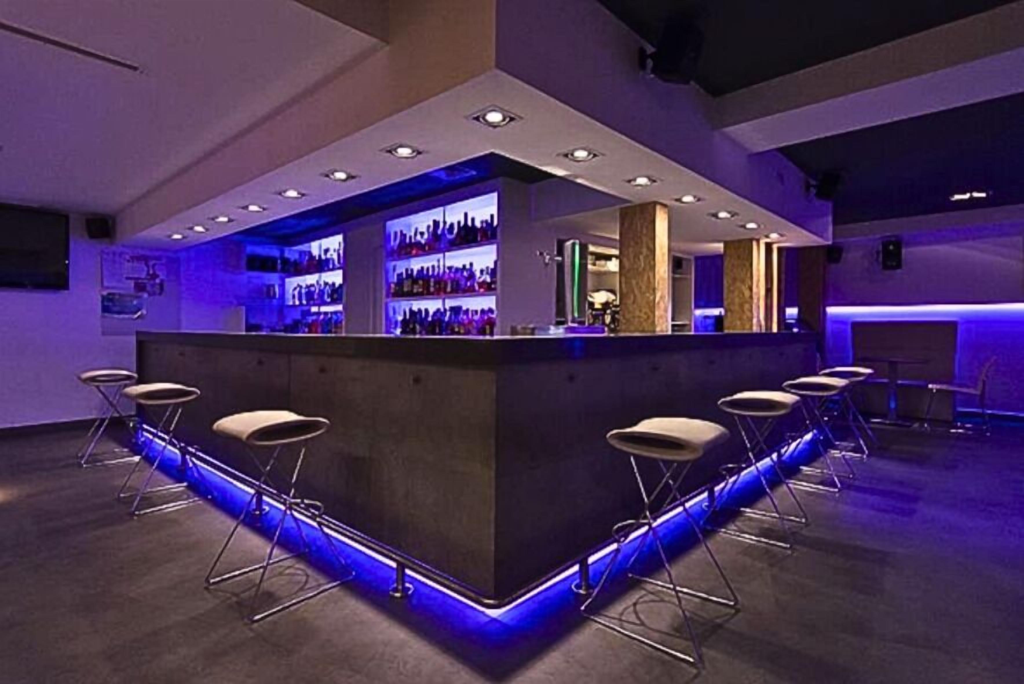 A bar area with a counter, bar stools, and shelves of bottles.