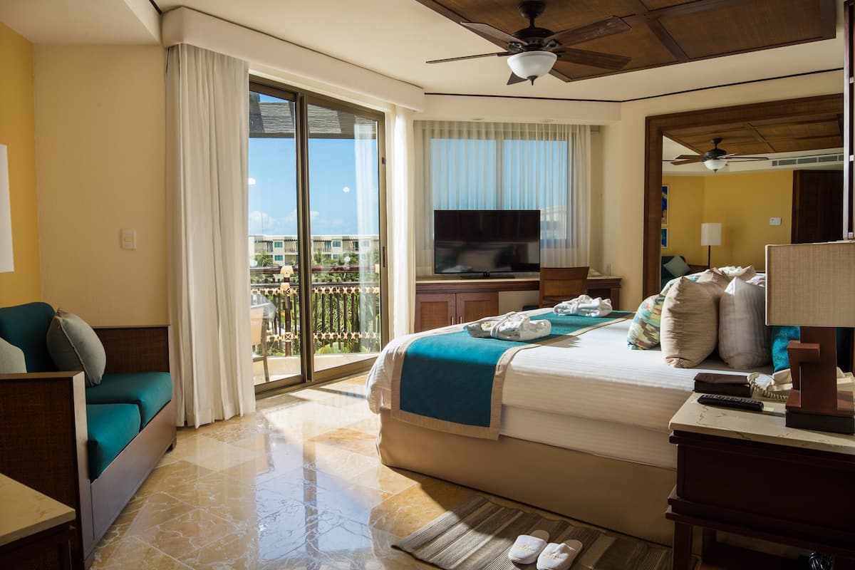 A hotel room with a bed, a TV, a balcony, and a ceiling fan.