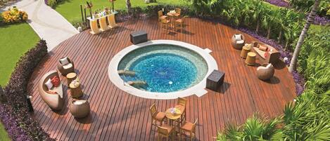 A circular outdoor area with a hot tub surrounded by wooden deck seating and a pool.