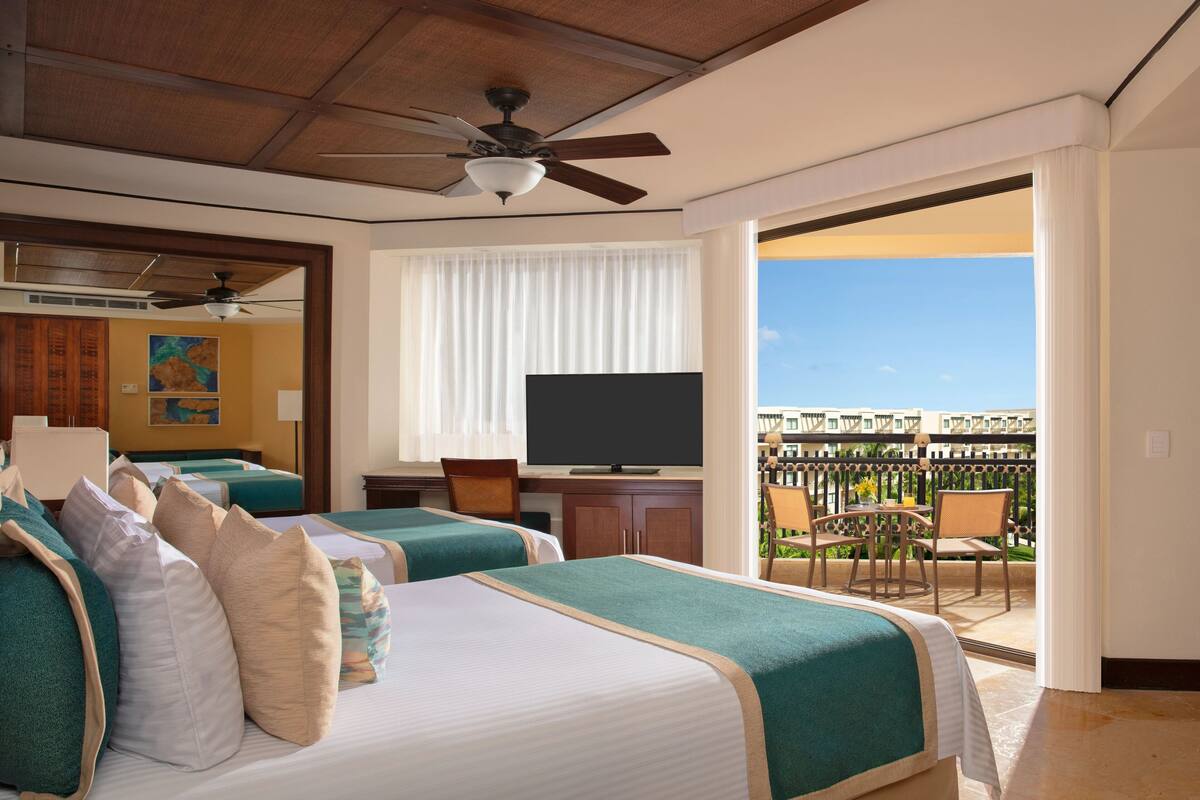 A hotel room with two beds, a TV, and a balcony with a view.