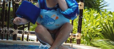 A child jumping into a pool wearing a blue life jacket with a shark design.
