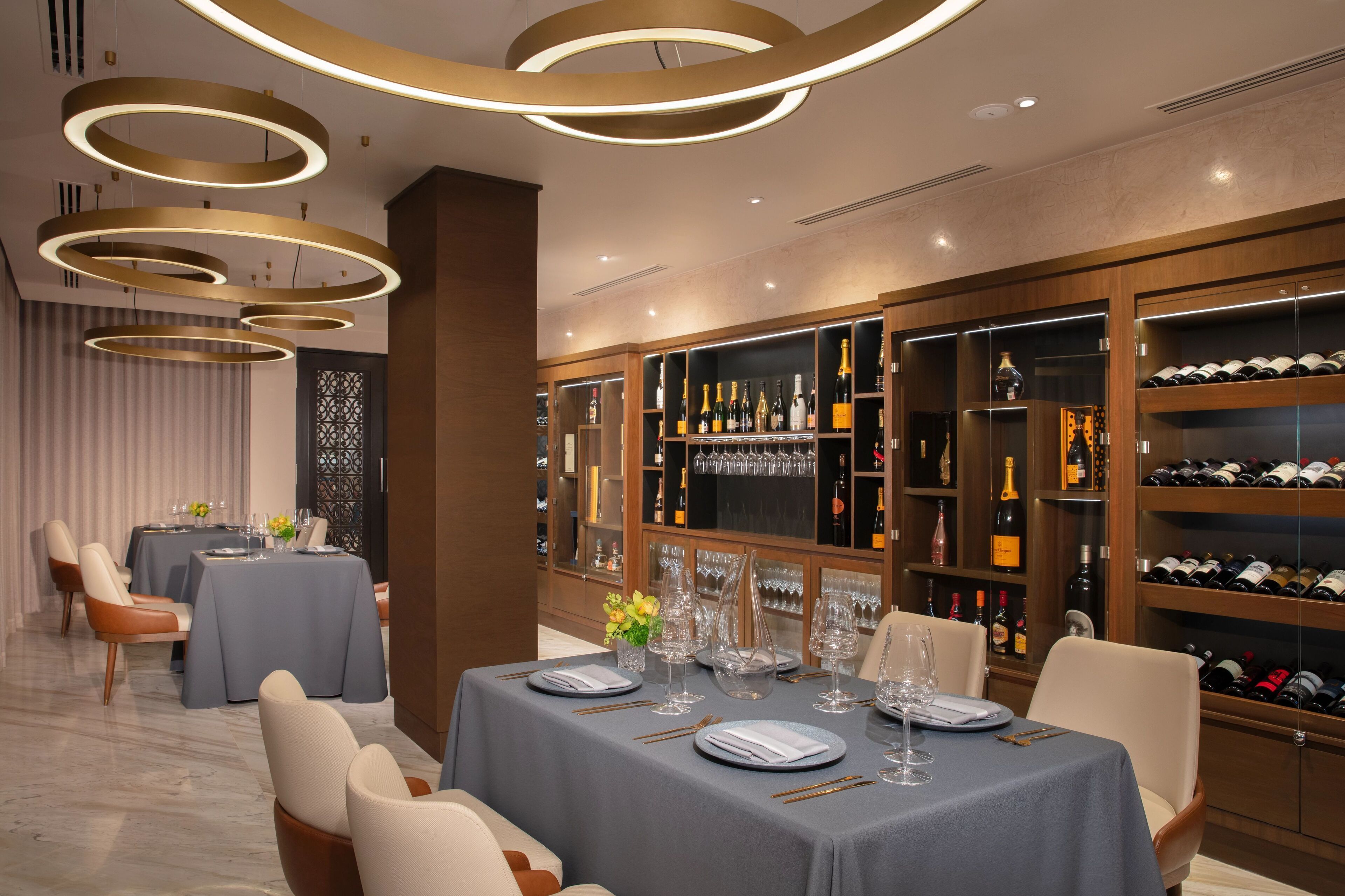 A restaurant with tables set for dining, a wine cellar with shelves of bottles, and a decorative ceiling light fixture.