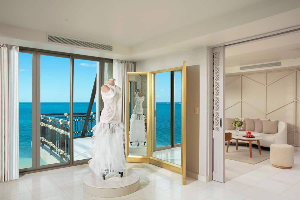 A spacious room with a large window offering a view of the sea, a white dress on a mannequin, a sofa, and a coffee table.