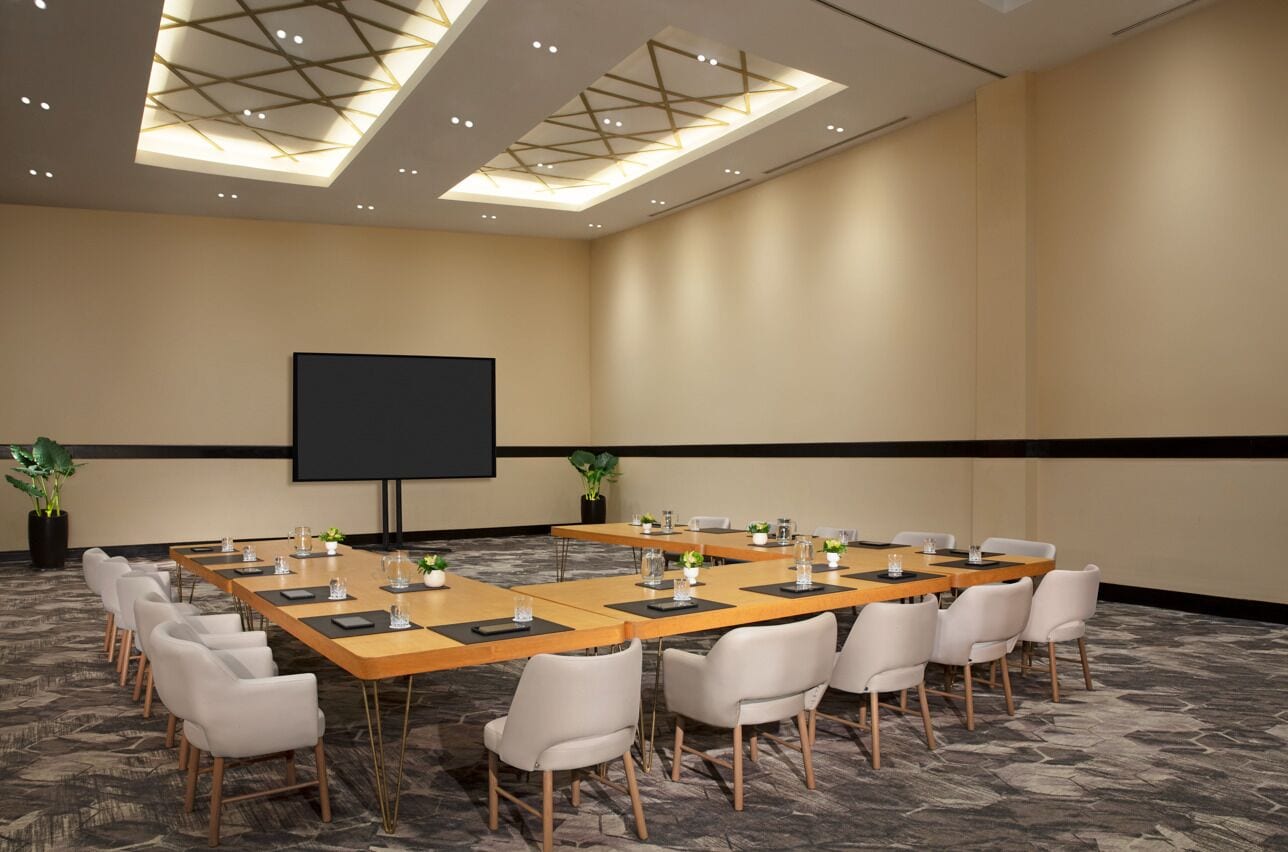A conference room with a large table, chairs, a projector screen, and ceiling lights.