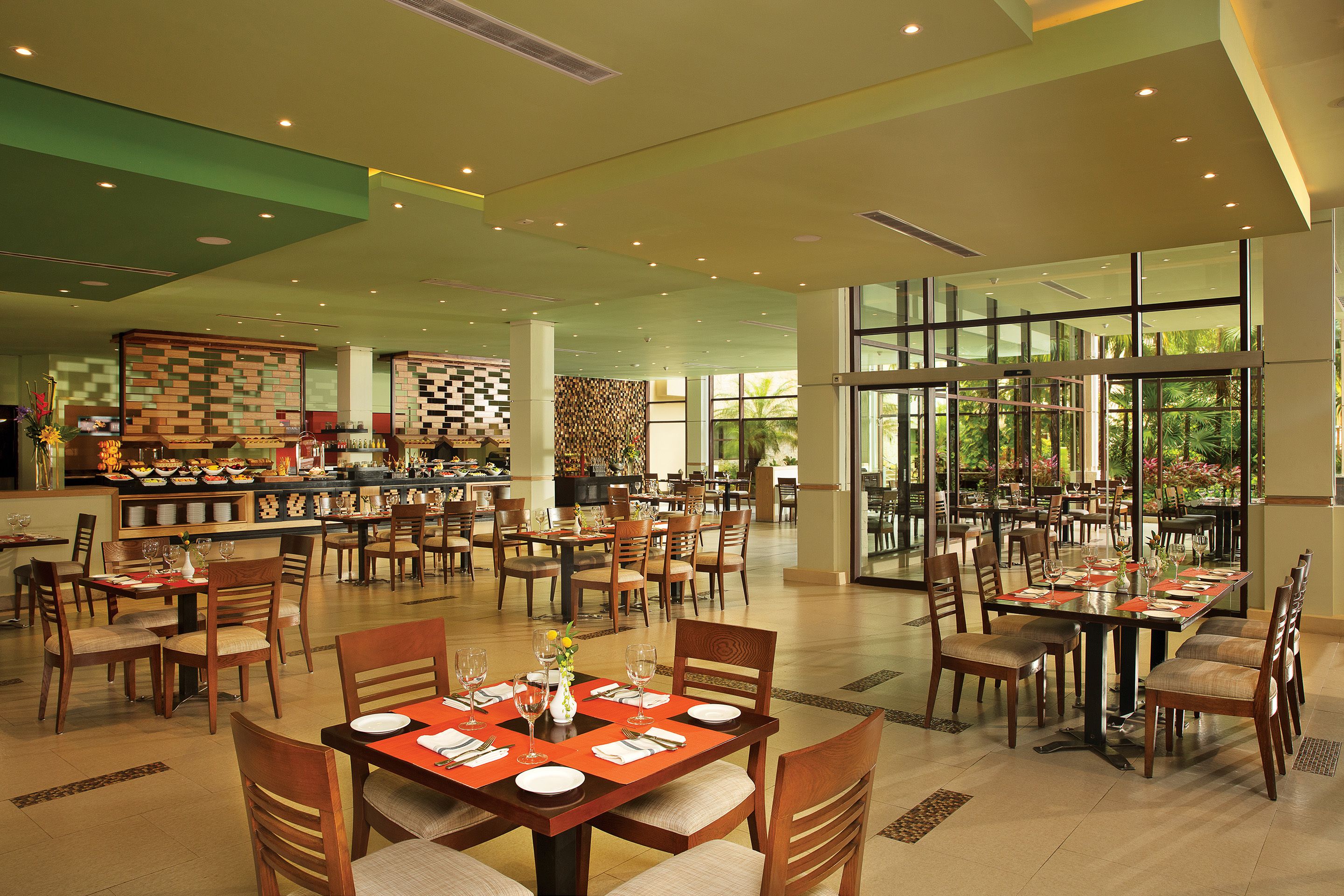 A spacious restaurant with multiple dining tables and chairs, a buffet area, and large windows offering a view of the outdoors.